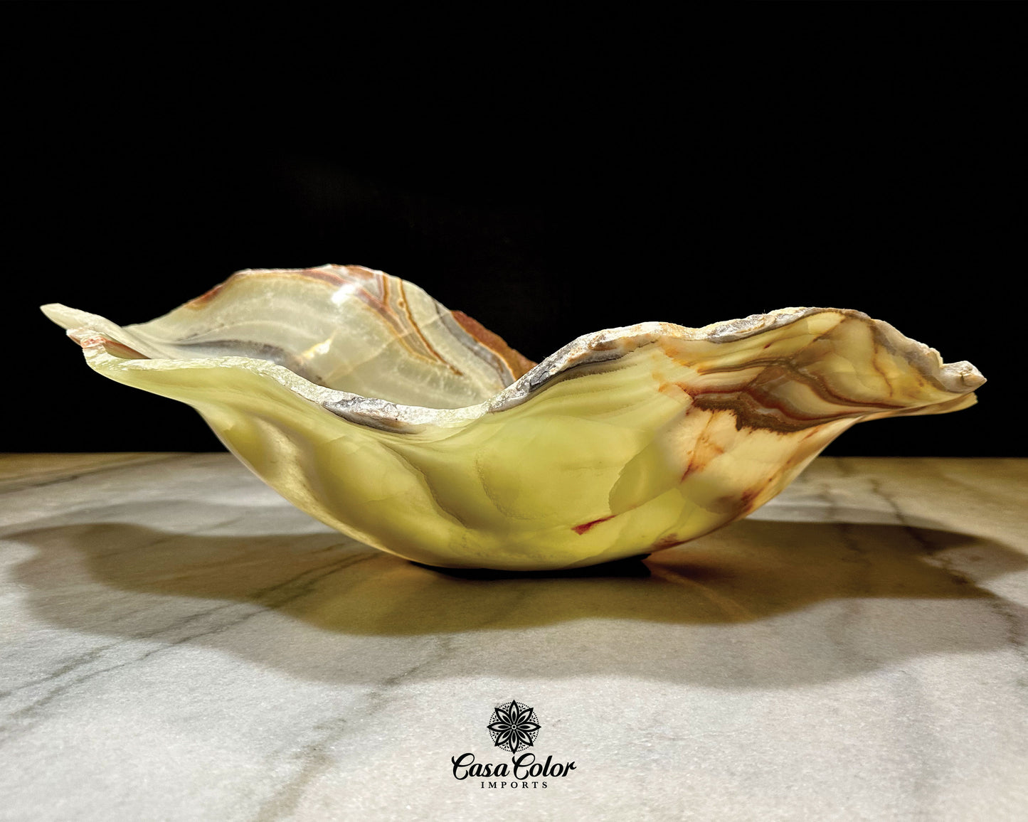 This bowl is one single hand-carved  piece of Onyx stone. This specific piece in particular has Polished Green Onyx crystal banded with beautiful red and brown veins with rough raw edges.  The size of this bowl is 26" long and 16" Wide. 