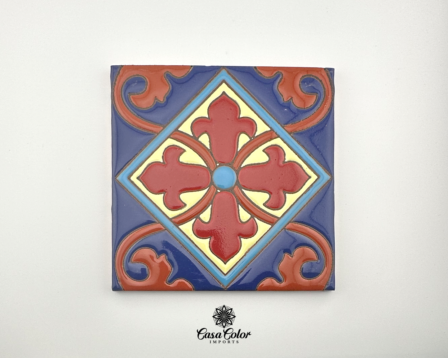 Handmade tiles 6x6. The color is glossy background blue with a flower in the middle in the shape of a cross. The flower is red/brown with long petals coming out from the center of the flower. The center of the flower has a blue dot. 