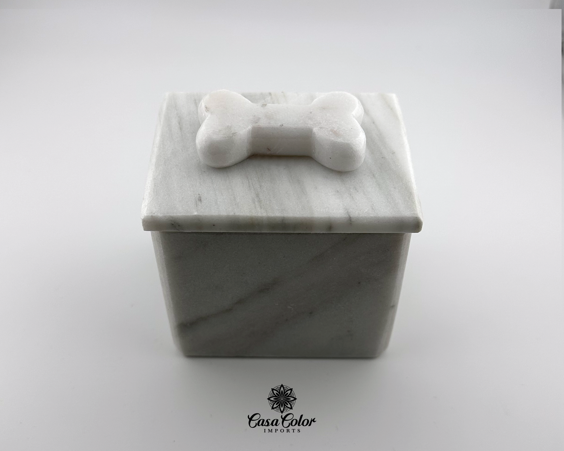 white dog urn for small dogs up to 25 lbs. 3 inches long, 3 inches wide and 3.5 inches high.  Urn is made of white Onyx with soft black veins. The urn has a bone shape on the top of the lid. The urn is square 